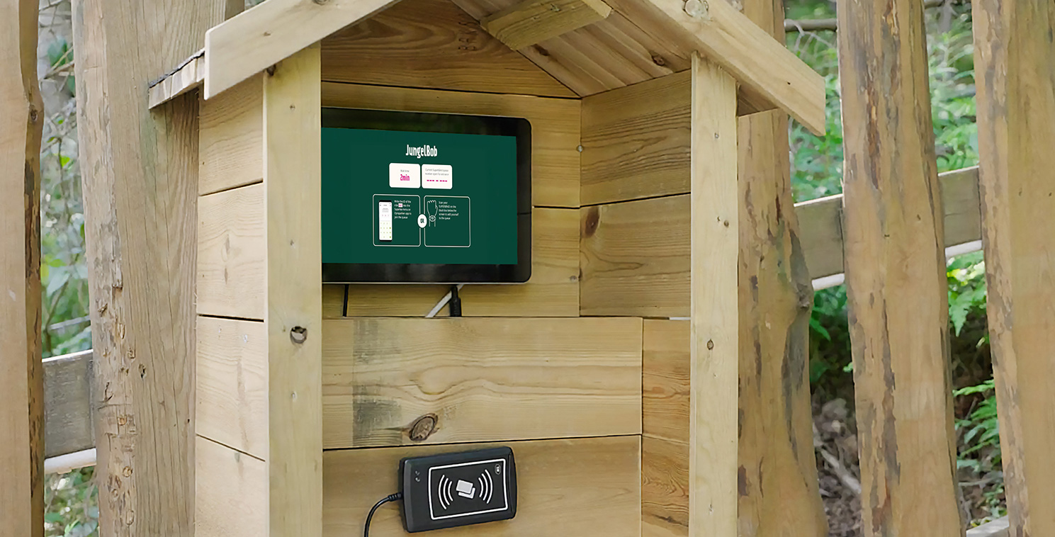 Outdoor Touchscreen Kiosk Enhancing Guest Experience at Amusement Park A visitor interacts with a weatherproof touchscreen kiosk housed in a wooden enclosure at an amusement park, showcasing self-service technology for ticketing.