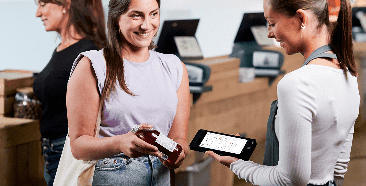 Two shoppers use a large touchscreen display in a retail store to explore virtual clothing options, showcasing experiential retail technology and personalized in-store engagement.